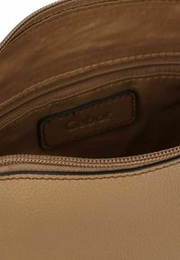 Das Innere der handgefertigten Tasche aus tanfarbenem Leder verfügt über einen Reißverschluss, eine glatte Textur und ein "Gabor"-Label auf einem Lederpatch. Schlichte Naht entlang der Kanten.