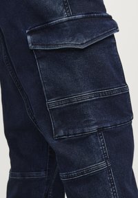 Pantalones cargo de denim azul oscuro con un diseño de múltiples bolsillos, que presentan detalles de costura, una textura suave y un ajuste estructurado.