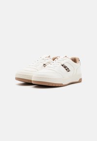 Des baskets blanches avec un dessus en cuir lisse, des accents beiges, une semelle en caoutchouc texturé et un motif léopard sur les côtés.