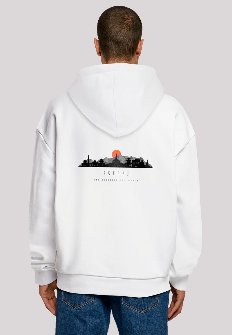 Man wearing white hoodie with black and orange mountain and city skyline graphic and text "ESCAPE AND DISCOVER THE WORLD" on the back.