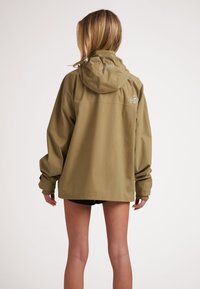 Giacca impermeabile color khaki con cappuccio, dotata di un logo sulla schiena, vestibilità rilassata e polsini elastici. Texture liscia e design minimale.