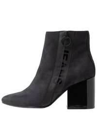 Botín negro de cuero de gamuza con un tacón bloque negro brillante. Cuenta con una cremallera lateral y un audaz logo "JEANS" en el lado exterior.