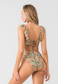 Jednodílné plavky s květinovým potiskem, ruffled ramínka, otevřený zadní design a zavazovací detail. Převážně zelené s oranžovými a béžovými akcenty.