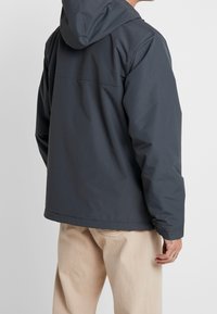 Grå, huva jacka med en slät, matt yta; har en avslappnad passform och kontrasterande sömmar, designad för komfort och mångsidighet.