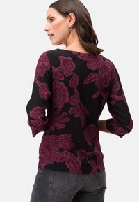 Top nero a maniche lunghe con grandi motivi floreali bordeaux, morbido al tatto, scollatura rotonda e spacchi laterali sull'orlo.
