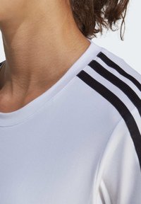 Wit sportshirt met zwarte horizontale strepen op de schouders, ronde halslijn en een gladde stoftextuur.