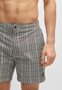 Heren zwembroek in een geometrisch zwart, wit en gouden patroon. Elastische tailleband met een knoopsluiting en een klein logo-label aan de zoom.