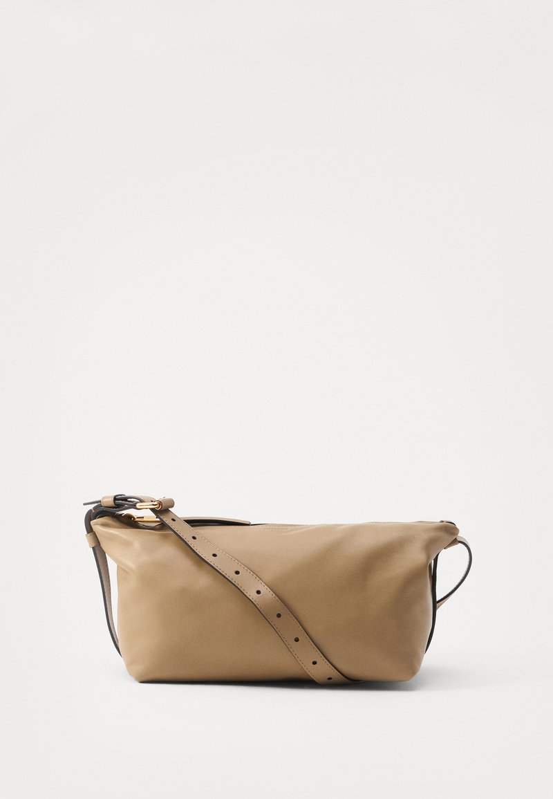 Sac en cuir beige avec une forme douce et décontractée, une bandoulière réglable, des détails en or et une texture lisse, présentant des éléments de design minimalistes.