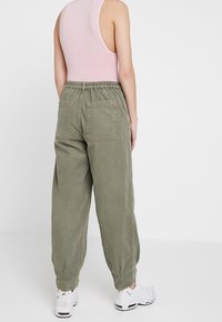 Light pink sleeveless top paired with loose, olive green cargo pants featuring elastic waistband and two back pockets. White sneakers visible.
