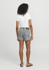 Shorts in denim bianco e nero con orlo sfrangiato, dotati di due tasche posteriori e una cintura con marchio, abbinati a una maglietta bianca.