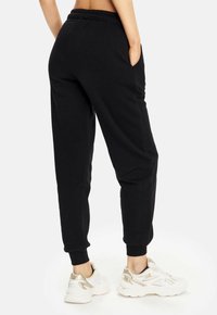 Schwarze Jogginghosen mit lässiger Passform, elastischem Bund und Seitentaschen. Die Bündchen an den Knöcheln sorgen für eine schmalere Silhouette. Kombiniert mit hellen Sneakers.