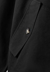 Tissu noir à texture lisse avec une poche dotée d'un rabat distinct et d'un bouton circulaire sur le côté droit. Design minimaliste.