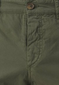 Pantaloni in cotone verde oliva con chiusura frontale a bottone, dettagli delle tasche cuciti e un tessuto liscio, leggermente strutturato.