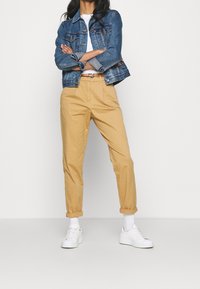 Veste en jean bleu foncé, t-shirt blanc, pantalon kaki fuselé, ourlets retroussés et baskets blanches. Tissu doux avec coupe décontractée.
