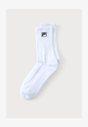 Paire de chaussettes blanches montantes avec des bords côtelés et un petit logo noir et blanc près du haut sur un fond neutre.