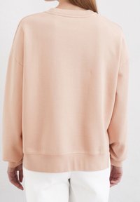 Felpa rosa con scollo a girocollo, spalle scese e polsini a coste. Tessuto liscio con vestibilità comoda, orlo inferiore rifinito.