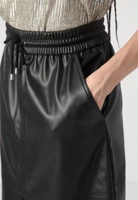 Černá kožená sukně s elastickým pasem, vybavená šňůrkou a bočními kapsami, hladká textura a elegantní design.