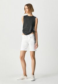 Top nero senza maniche con cucitura frontale e lacci laterali regolabili abbinato a pantaloni corti in denim bianchi. La modella indossa sneakers bianche.