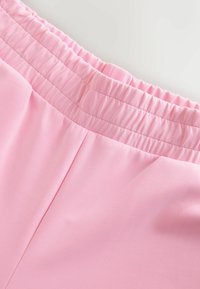 Hele roosa elastne vöökoht, millel on kortsus tekstuur, kinnitatud siledale kangale, millel on lame esiosa ja küljeõmblused. Taskuid ei ole nähtaval.