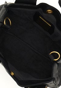 Interno di una borsa in pelle nera con una fodera in tessuto texturizzato, dotata di hardware dorato e una tasca laterale con un'etichetta scura.
