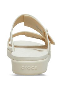 Beige Crocs sandals with a smooth texture, featuring two adjustable straps and a contoured footbed, have a chunky sole with logo detail.
