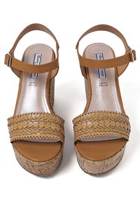 Sandali platform in pelle color cuoio con cinturini intrecciati, tacco in sughero e fibbie alla caviglia. Superficie liscia con perforazioni decorative sulla parte superiore.