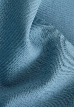 Tessuto di tessile blu chiaro che mostra una superficie liscia e morbida con sottili trame a maglia e un'accennata caduta, illustrando flessibilità e comfort.
