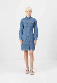 Jeans haljina, plava, s dugim rukavima, patentnim prednjim dijelom, dva džepa na grudima i ukrasnim zakovicama na ramenima.