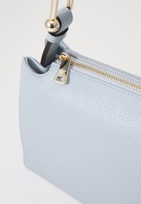 Borsa a mano in pelle blu chiaro con superficie testurizzata, zipper dorato e un accento in hardware lucido. Forma rettangolare compatta con tracolla regolabile.