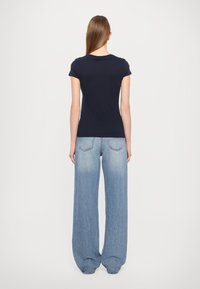 Námořnické bavlněné tričko s krátkým rukávem, spárované se světle modrými kalhotami s širokými nohavicemi, s klasickým pětibokým designem a vybledlým vzhledem.