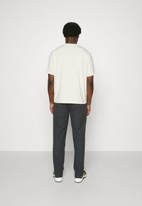 Hellgraues Kurzarm-T-Shirt kombiniert mit dunklen Hosen, im entspannten Schnitt und minimalistischen Design, von hinten angesehen.