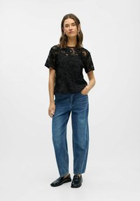 Sort blondebluse med blomsterbroderi, korte ærmer, rund halsudskæring. Kombineret med lyseblå højttaljede jeans med lige ben og sorte sko.