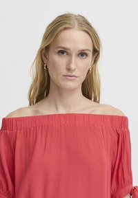 Blusa rossa a spalle scoperte con texture stropicciata, maniche corte e scollatura elastica. Tessuto morbido, design casual e vestibilità rilassata.