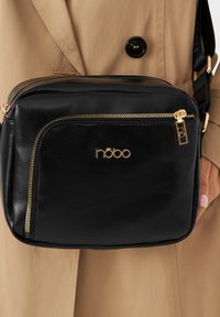 Borsa a tracolla in pelle sintetica nera con finiture dorate, scomparti con zip e logo in rilievo. Forma rettangolare compatta.