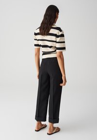 Haut en tricot à manches courtes avec des rayures crème et noires ; associé à un pantalon large noir avec des ourlets retroussés ; sandales à brides beiges.