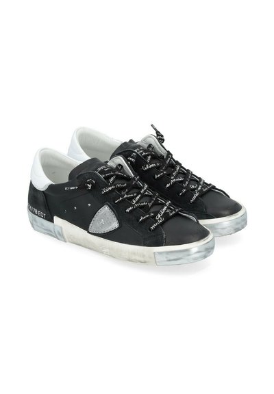 Baskets noir et blanc avec une tige en cuir et en daim, dotées de accents gris, de lacets texturés avec du texte blanc et d'une semelle en caoutchouc usée.