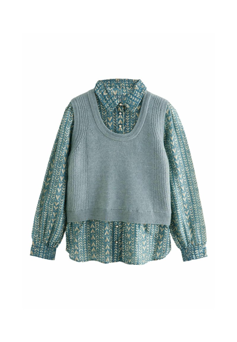 Chemise à manches longues à motifs bleu sarcelle avec col, boutonnée, portée sous un gilet sans manches gris clair en maille.