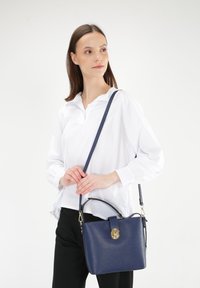 Navy leather handbag with pebbled texture, top handle, and adjustable shoulder strap. Features a gold clasp closure and minimalist design.
