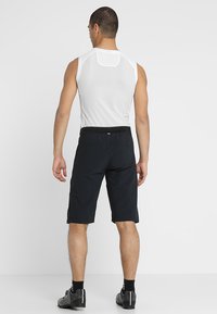 Sporty sleeveless shirt in white mesh fabric, paired with dark black shorts. The shorts feature an elastic waistband and a relaxed fit.
