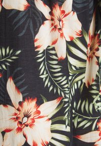 Květinová látka s velkými krémovými a oranžovými květy se červenými akcenty na tmavém pozadí, obklopená zelenými listy a kapradinami.