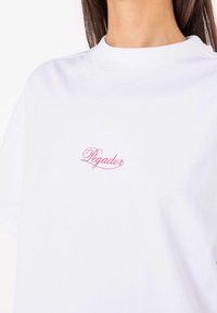 White cotton t-shirt featuring a pink cursive "Pegador" logo on the left chest. The design includes a crew neckline and short sleeves.