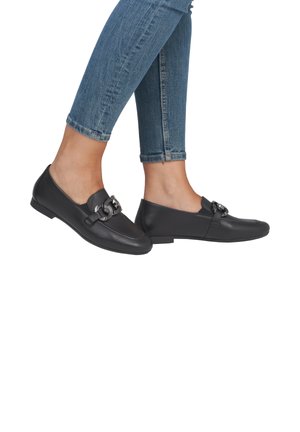 Zwarte lederen instappers hebben een vierkante neus, een decoratieve gespaccent en een platte zool, gecombineerd met lichtblauwe skinny jeans.
