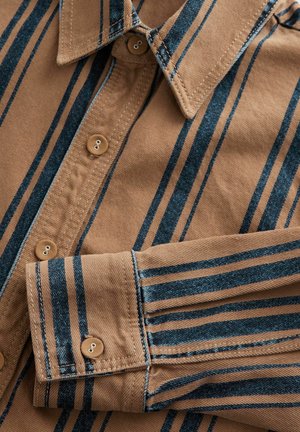Chemise rayée brun avec des lignes verticales bleues, col boutonné, et deux boutons sur le plastron. Tissu lisse avec des détails de couture fins.