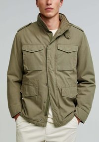 Olive green military-style jacket with a high collar, two chest pockets, and two lower pockets. Made of durable fabric, button and snap closure.