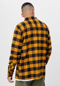 Geel en zwart geruit overhemd met knopen, gemaakt van flanel, met een relaxte pasvorm, lange mouwen en een label aan de zijkant.