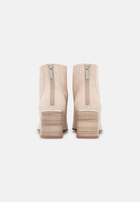 Botines de ante beige con un alto tacón apilado, que presentan una cremallera en la parte trasera y una textura suave con un patrón sutil en el tacón.