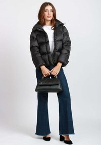 Giacca a vento nera con collo alto, design trapuntato, abbinata a pantaloni in denim svasati e una piccola borsa nera con dettagli a catena.