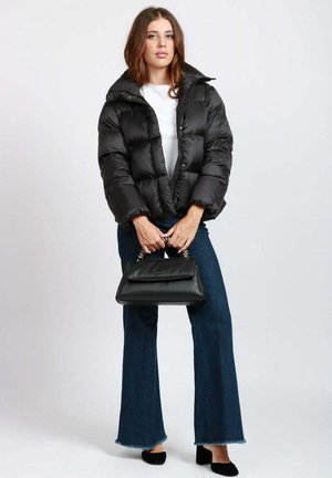 Giacca a vento nera con collo alto, design trapuntato, abbinata a pantaloni in denim svasati e una piccola borsa nera con dettagli a catena.