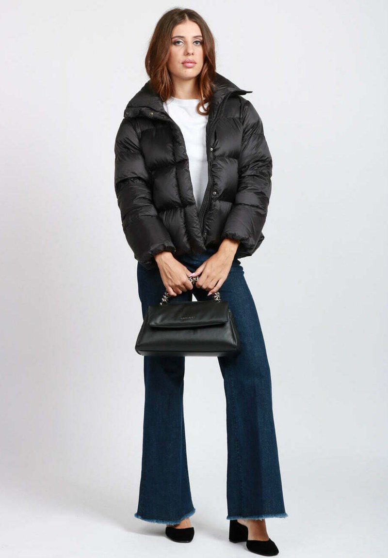 Giacca a vento nera con collo alto, design trapuntato, abbinata a pantaloni in denim svasati e una piccola borsa nera con dettagli a catena.