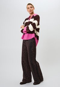 Ruskea ja valkoinen raidoitettu neule pitemmillä hihoilla, jossa on vaaleanpunainen kaulus, yhdistettynä leveälahkeisiin housuihin, joissa on tumma eläinkuos. Sujuva pinta ja rento malli.